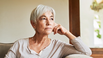 Old and gray haired woman with Alzheimer's sitting alone at a sofa with a thoughtful look