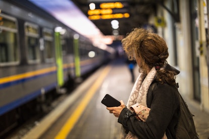 A woman holding her phone standing at a train station