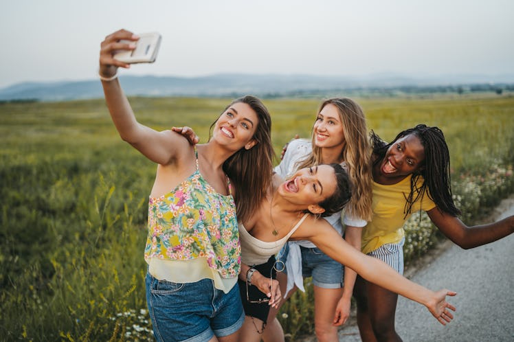 Four young women take a funny selfie while standing next to a grassy field.
