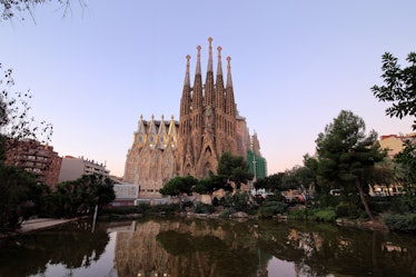 Basilica de la Sagrada Familia in Barcelona, Spain stands tall over a pond at sunset.