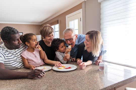 multicultural family sitting at kitchen island, little girl feeding grandpa dessert