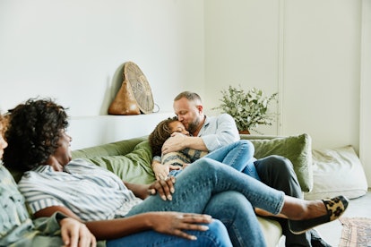 A dad hugs his daughter while sitting on a green couch with their other family members.