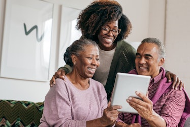 A young Black woman stands with her parents and laughs while they look at a tablet.