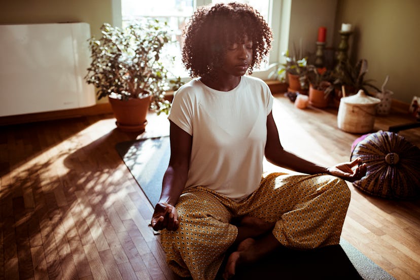 A woman meditates in a sun-dappled room. The Fitness Industry Needs To Confront Its Structural Racis...