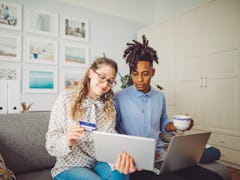 A young couple online shops on a tablet while sitting on a couch in their home.