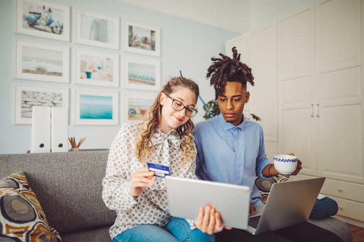 A young couple online shops on a tablet while sitting on a couch in their home.