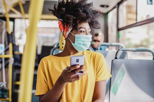 A woman looks out the window of a bus wearing a face mask. How To Handle Anxiety About Going Back To...