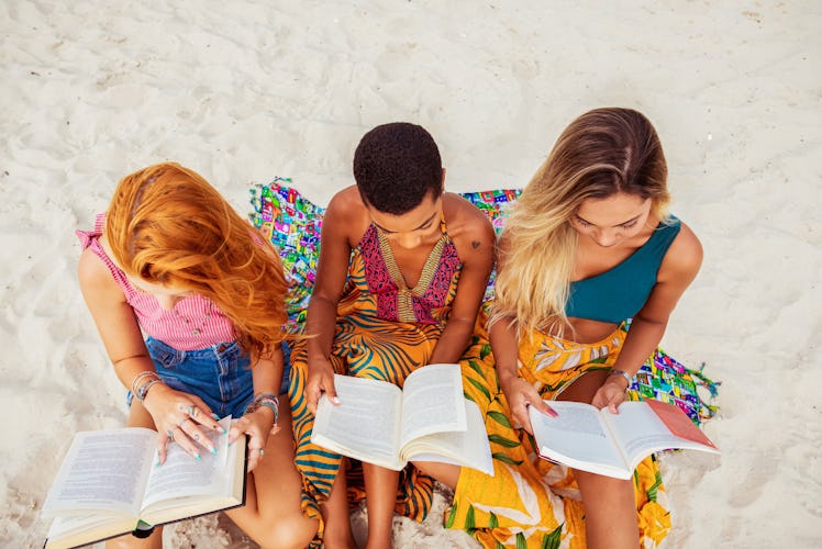 Three young women sit on the beach and read books in the middle of summer.