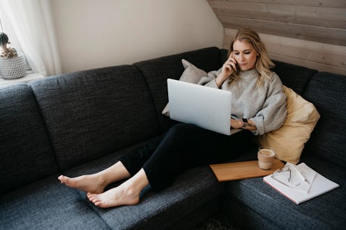 A woman works from her couch. These 13 stretches to fix working from home aches and pains can allevi...