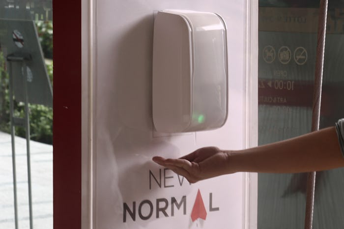 person holding hand under hand sanitizer dispenser