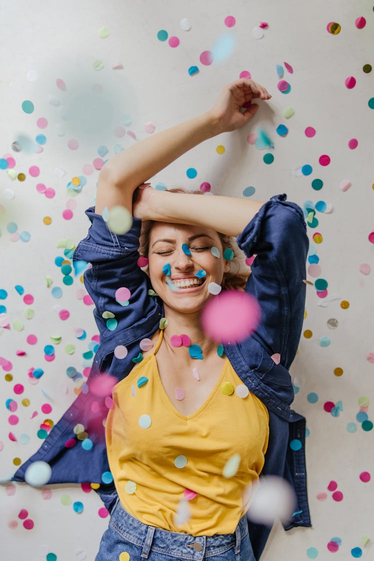 A young woman dances in confetti while somebody takes her picture on her birthday.