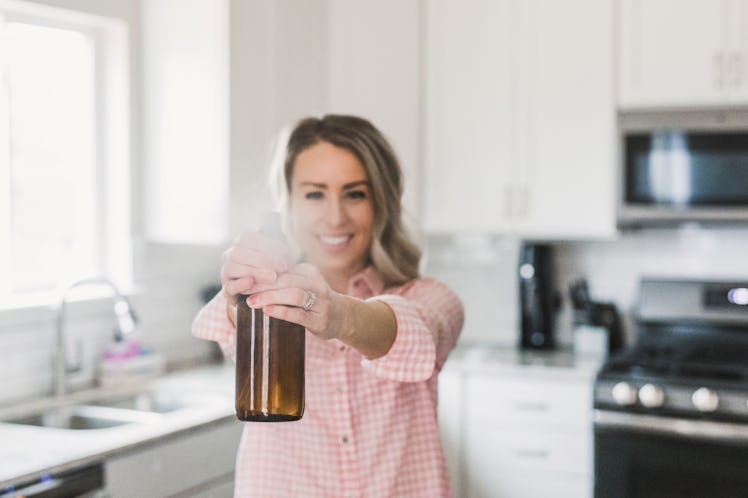 A happy woman in her kitchen holds a spray bottle up. 