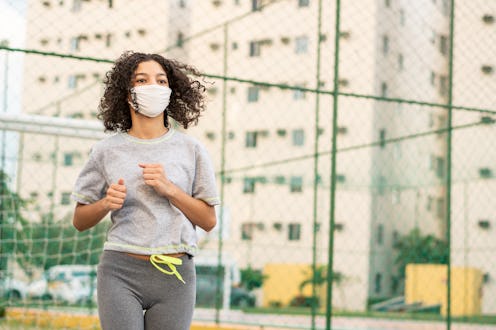 A person wearing a grey short-sleeved running tee goes for a jog outside while wearing a mask. You m...