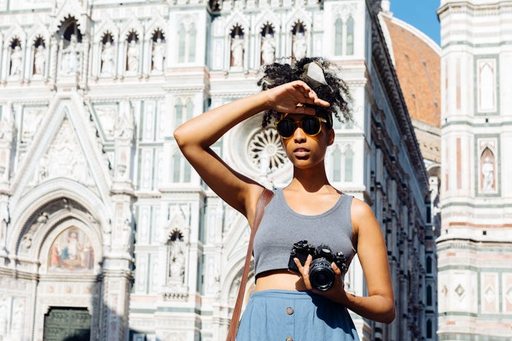 A young Black woman stands in front of the Duomo in Florence, Italy with her camera on a sunny after...