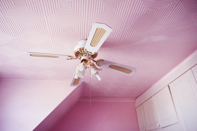 A fan on the plafond of a room with pink walls