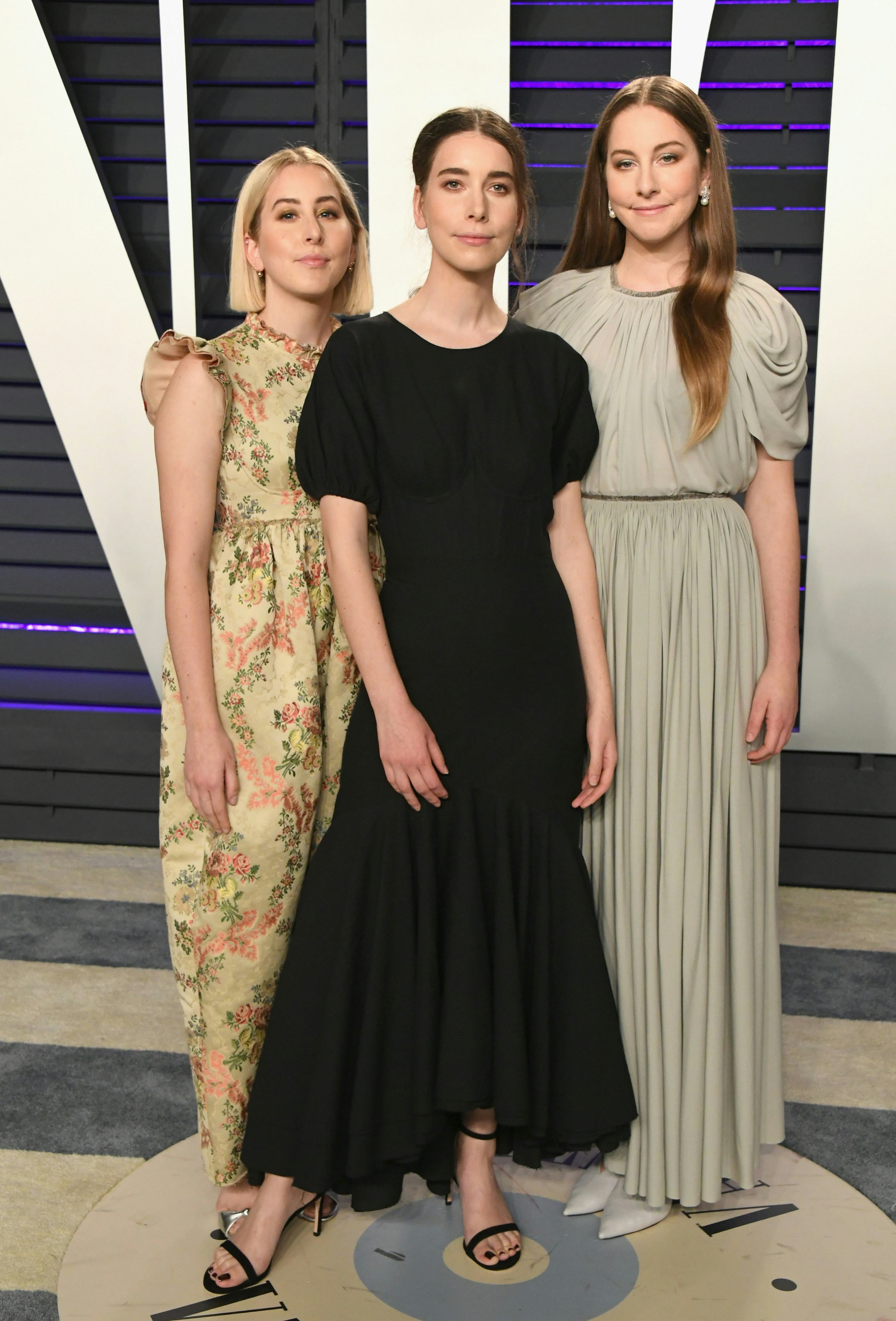 Alana Haim, Danielle Haim and Este Haim of HAIM wearing black, yellow and light brown dresses