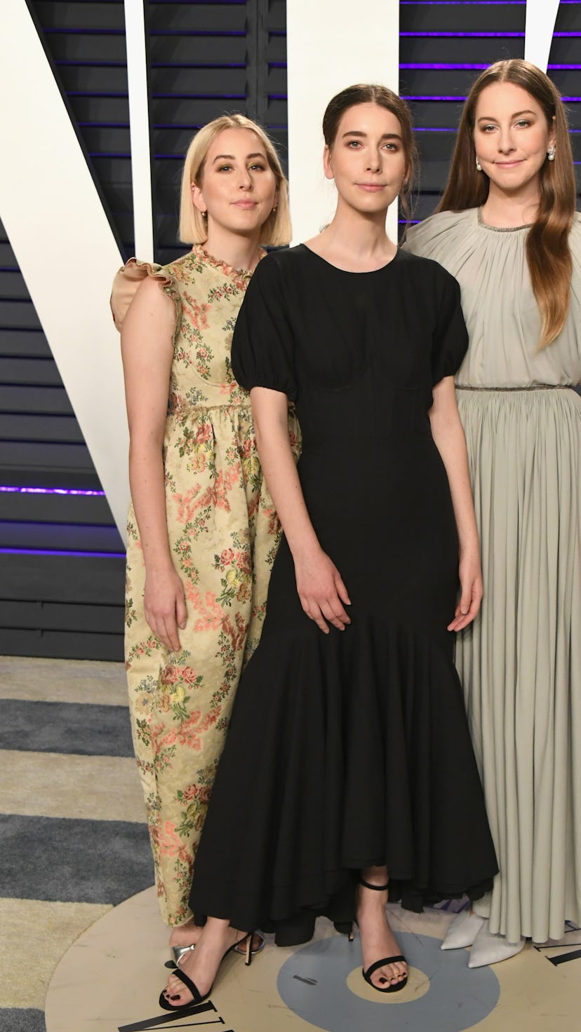Alana Haim, Danielle Haim and Este Haim of HAIM wearing black, yellow and light brown dresses