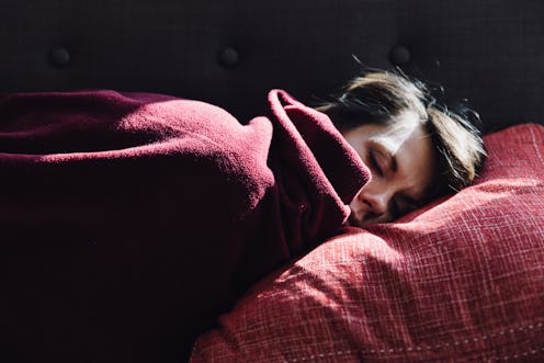 A woman sleeps under a red blanket. Experts Explain How Apple’s New Sleep Tracking Feature Can Affec...