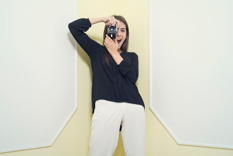 A young woman poses in front of a white and yellow backdrop with her digital camera.