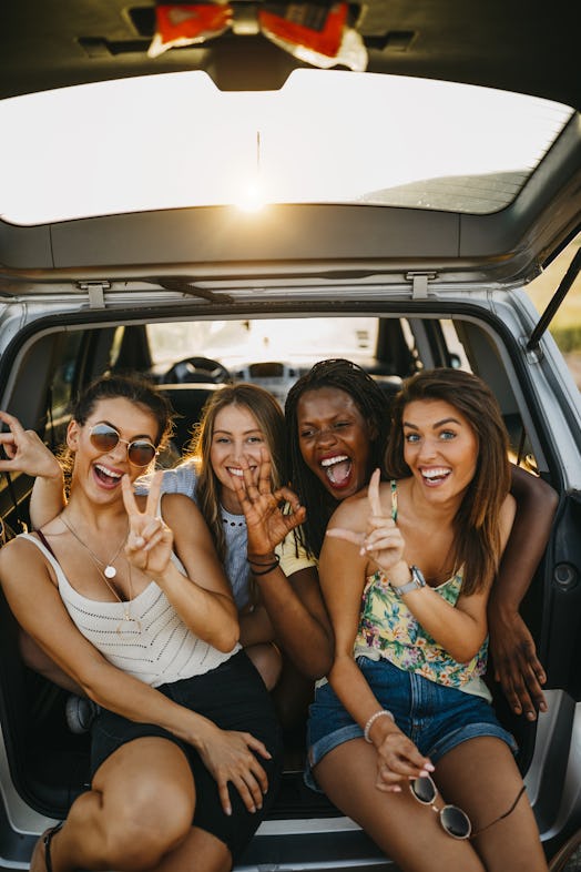 Four women hang out in the trunk of a car at sunset and pose for the camera.