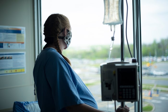 pregnant woman looking out window at hospital wearing mask