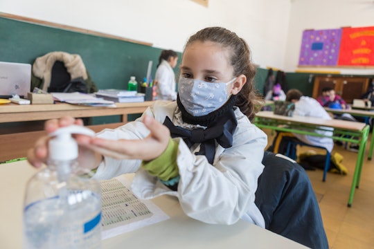 girl in face mask sanitizes her hands at school