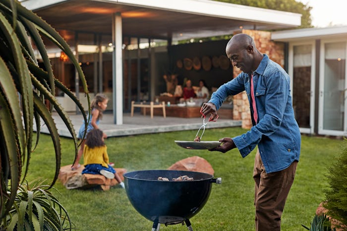 a black dad grilling in the backyard with kids sitting on lawn