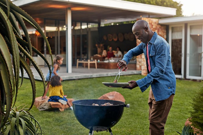 a black dad grilling in the backyard with kids sitting on lawn 