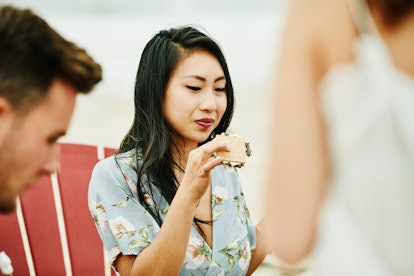 A young Asian woman sits in a beach chair and eats a s'more.