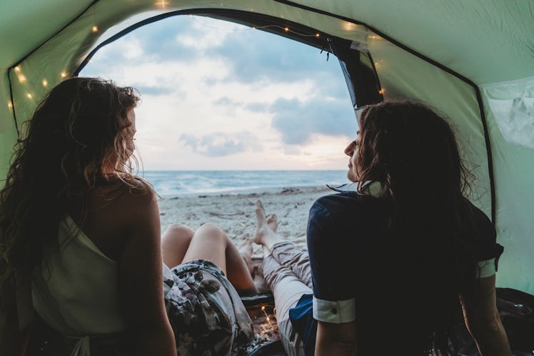A lesbian couple sits in a tent on the beach and stargazes.