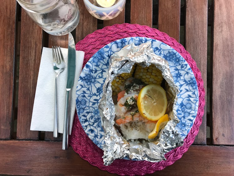 A grilled foil wrap sits on a colorful place setting on an outdoor dining table.