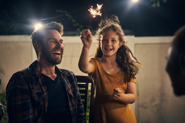 A dad and daughter laughing while they set off fireworks in their backyard