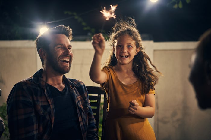 A dad and daughter laughing while they set off fireworks in their backyard