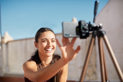 A young woman smiles while setting up her video camera outdoors on a tripod.