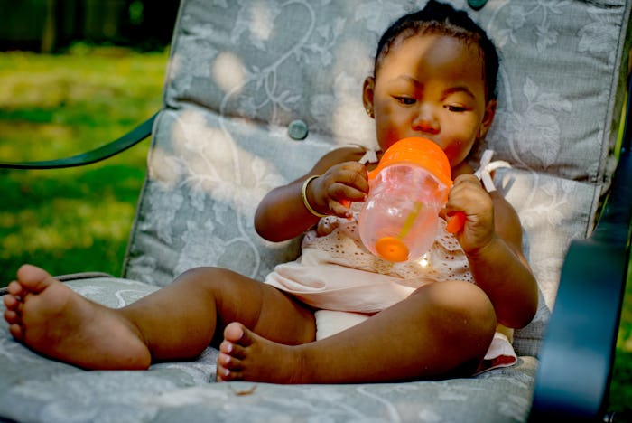 black baby girl sitting on chair outside with sippy cup