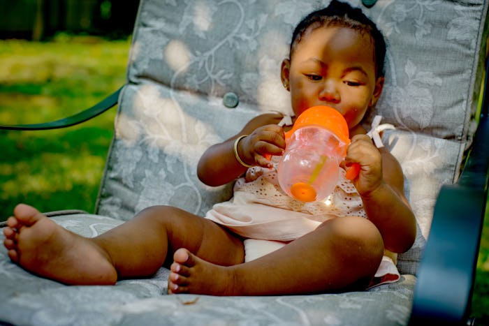 black baby girl sitting on chair outside with sippy cup