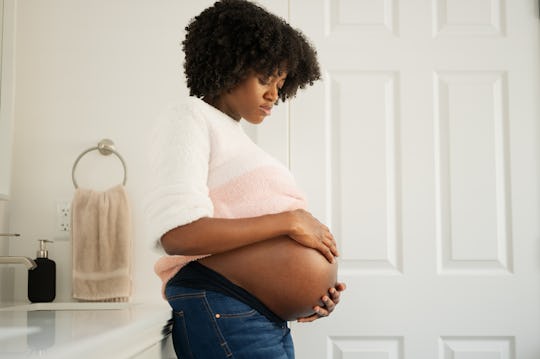 a black woman holding her belly in the bathroom