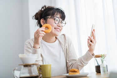 A young woman poses during a video chat with an old fashioned doughnut.