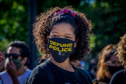 African-American woman with a face mask that says defund police, protesting against police brutality...