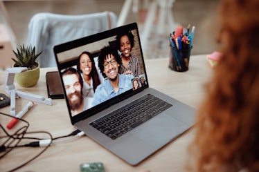 A family smiles into a video chat on their laptop, and poses for a picture.