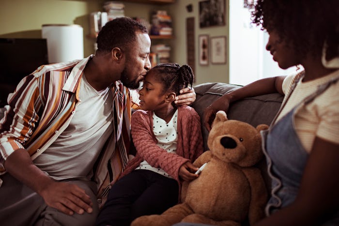 a Black mom and dad on couch with daughter and teddy bear