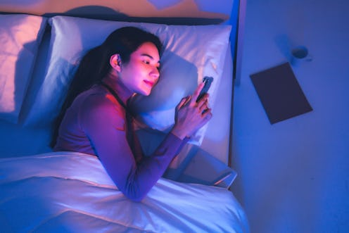 A woman on her phone in bed at night using dark mode.