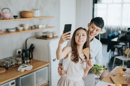 A young couple poses for a selfie while cooking a healthy meal together.
