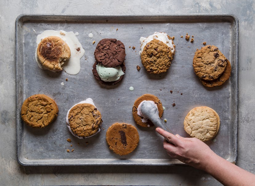 A person putting scoops of ice cream on cookies on a baking tray, to make ice cream sandwiches