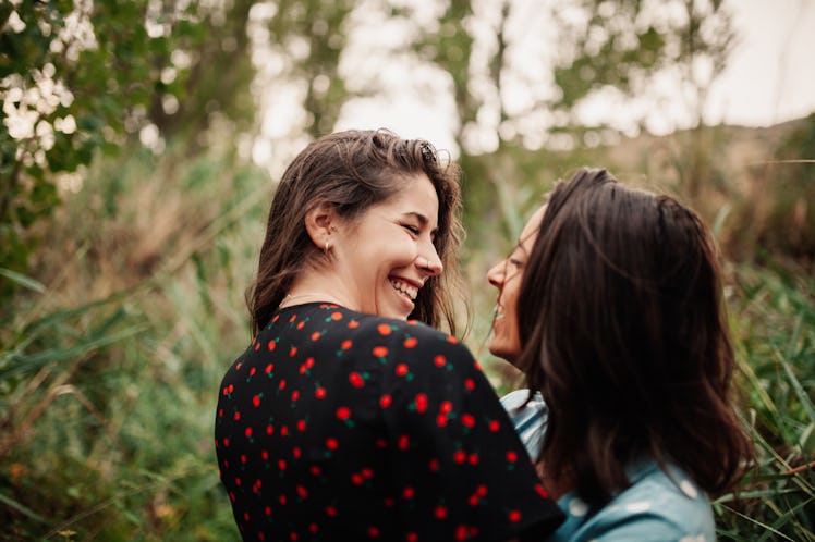 A young lesbian couple poses for a picture in a lush field and laughs.