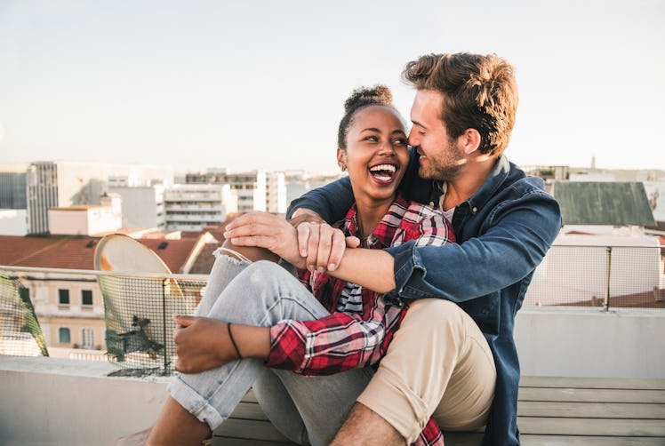 A young couple laughs while sitting on their rooftop and waiting for a sunset.