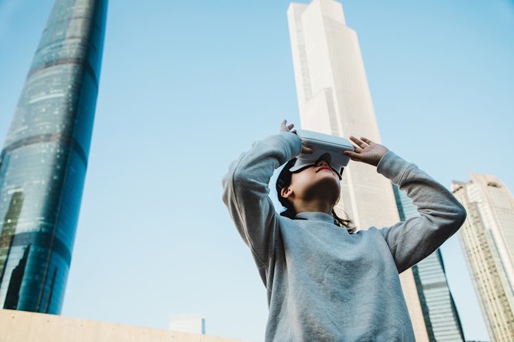 A young woman stands in the middle of a city on a sunny day and plays with a virtual reality headset...