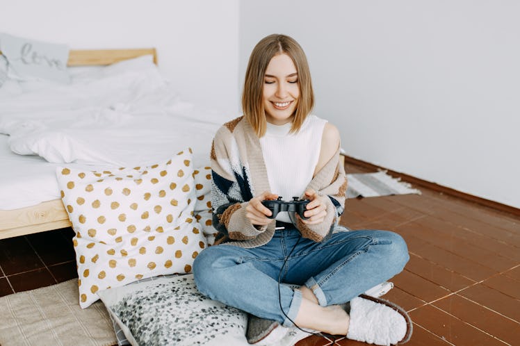A young woman smiles while playing video games in her room.