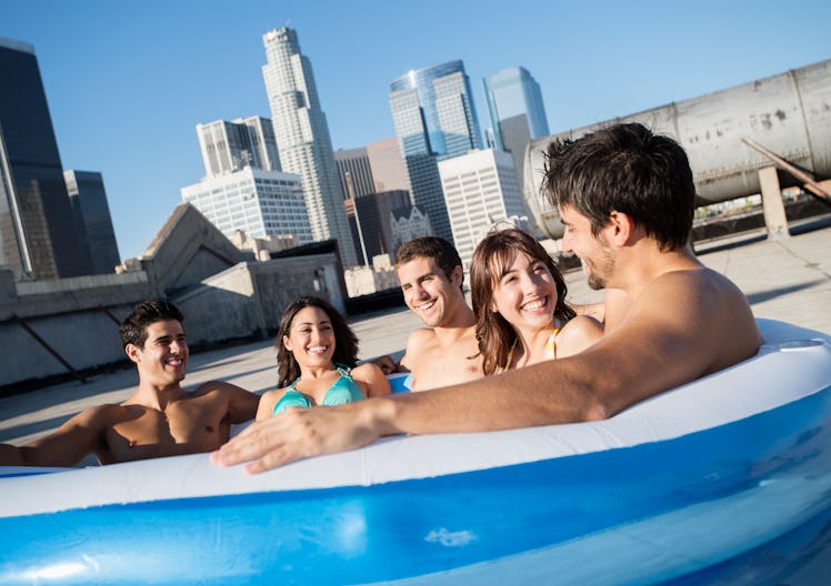 A group of friends sit in an inflatable pool on the roof. 