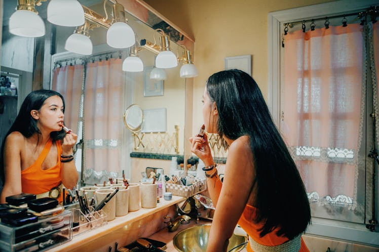 A young woman does her makeup in a vintage-looking bathroom mirror.